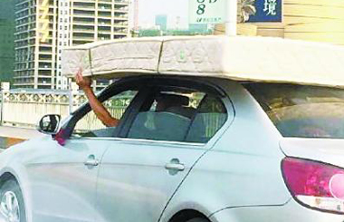 轿车车顶驮床垫飞驰 司机右手开车左手扶垫