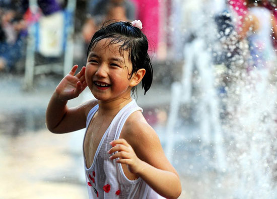 7月3日,一名女孩在辽宁沈阳街头的喷泉旁玩水纳凉.