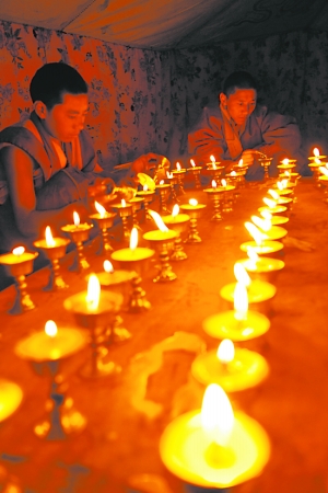 两名僧人在地震废墟前点亮酥油灯盏(图)