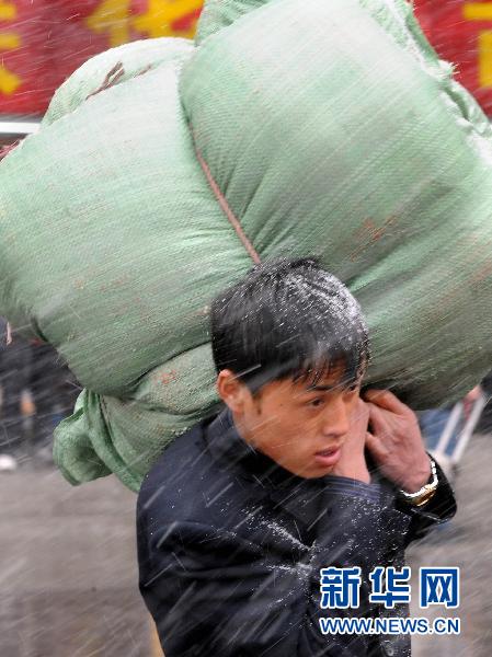 2月9日,一位扛着大件行李的旅客冒雪走在前往车站的路上.