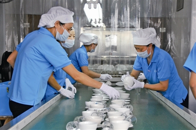 消毒中心员工将消毒完成的餐具摆放整齐,准备覆膜包装.